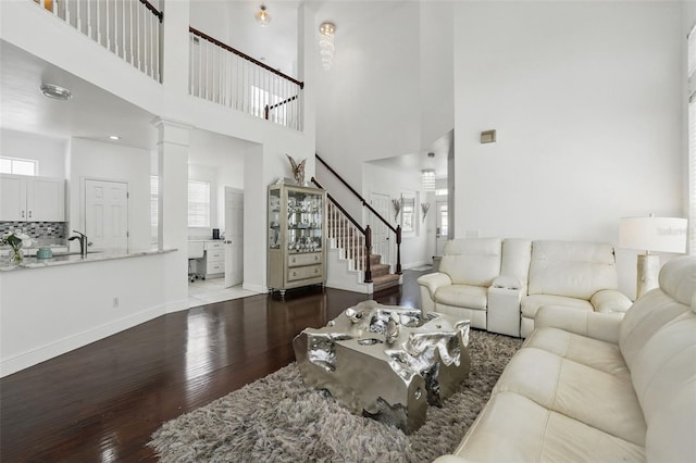 living room featuring stairway, wood finished floors, baseboards, decorative columns, and a towering ceiling