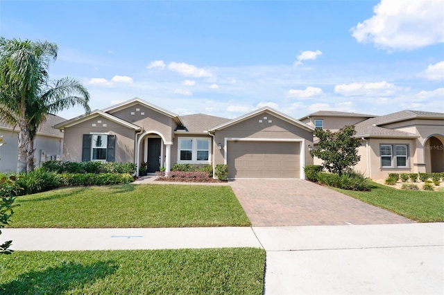 view of front of house featuring stucco siding, an attached garage, decorative driveway, and a front lawn