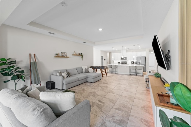 living room featuring a tray ceiling and visible vents