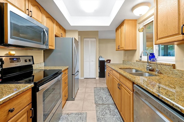 kitchen featuring a sink, appliances with stainless steel finishes, light tile patterned flooring, a raised ceiling, and light stone countertops