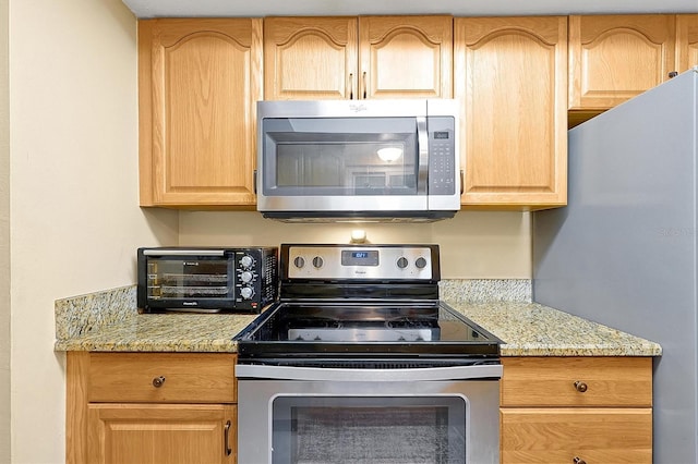 kitchen featuring light stone countertops, appliances with stainless steel finishes, light brown cabinetry, and a toaster