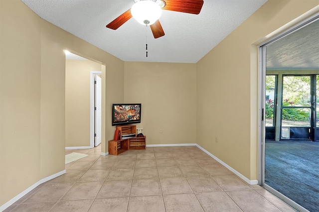 empty room with ceiling fan, light tile patterned floors, baseboards, and a textured ceiling