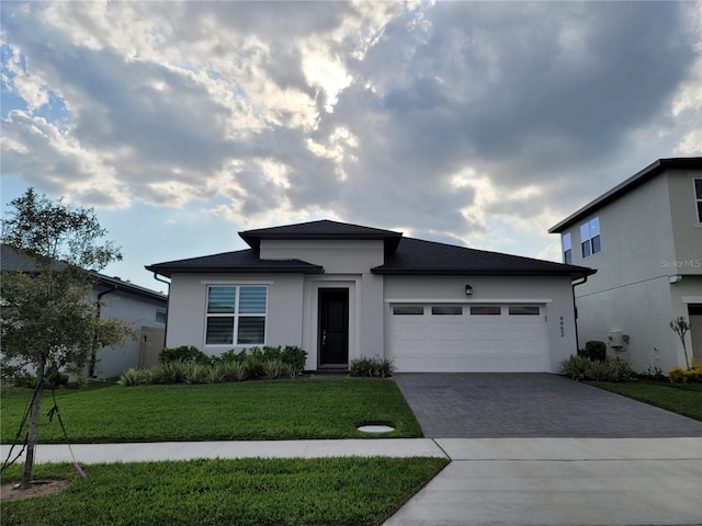 prairie-style home with stucco siding, an attached garage, decorative driveway, and a front lawn