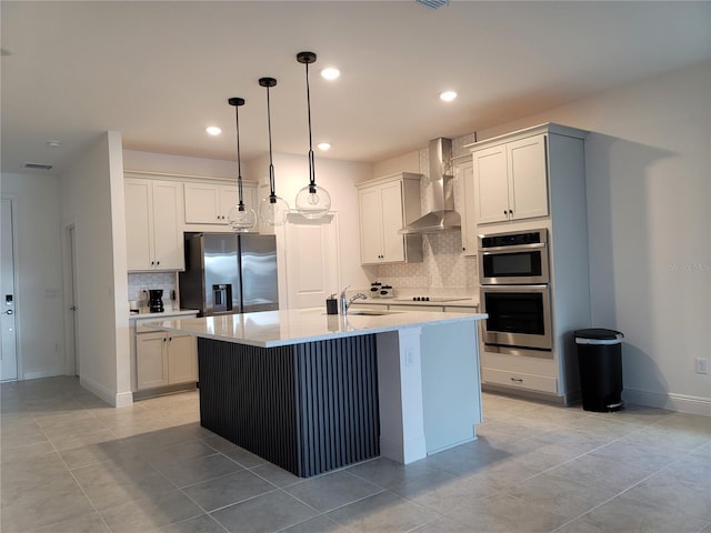 kitchen with a center island with sink, a sink, stainless steel appliances, wall chimney range hood, and decorative light fixtures