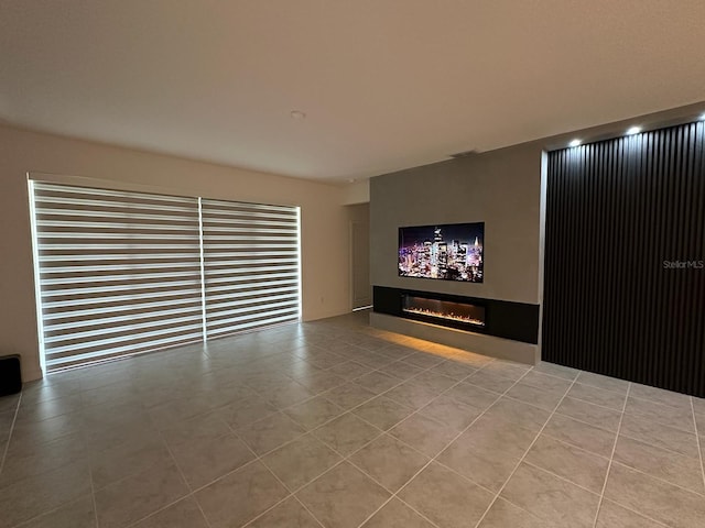 unfurnished living room featuring a glass covered fireplace and tile patterned flooring