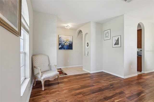 sitting room featuring arched walkways, baseboards, and wood finished floors