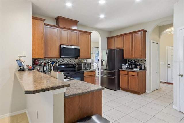 kitchen with arched walkways, brown cabinets, appliances with stainless steel finishes, and a peninsula