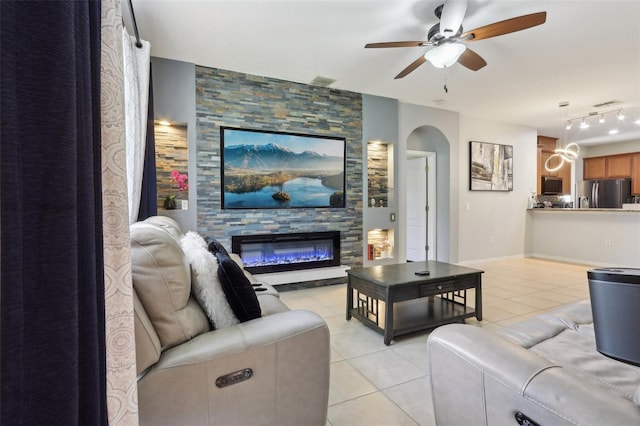 living area featuring visible vents, a stone fireplace, arched walkways, light tile patterned flooring, and a ceiling fan