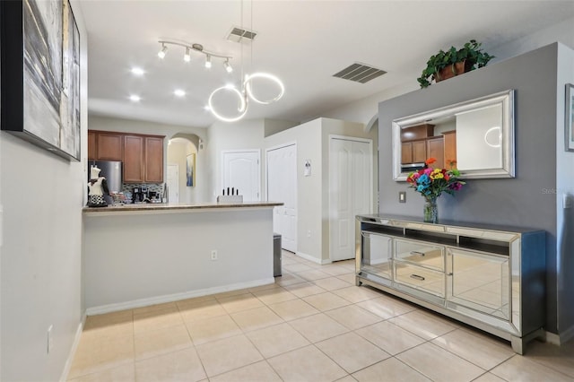 kitchen featuring visible vents, backsplash, brown cabinetry, light tile patterned floors, and arched walkways