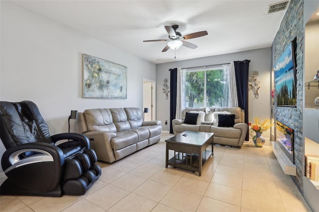 living room with a stone fireplace, light tile patterned floors, a ceiling fan, and visible vents