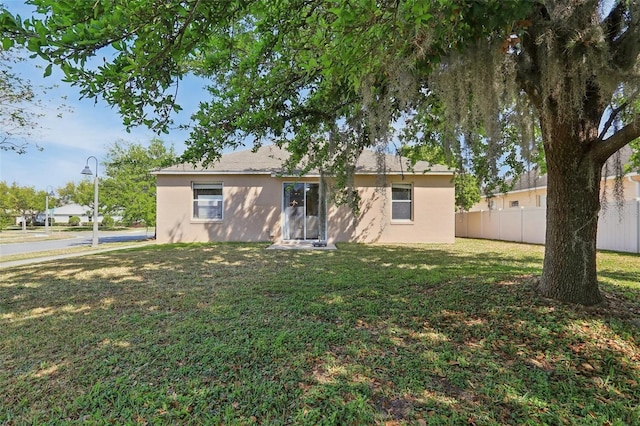 back of property with a yard, fence, and stucco siding