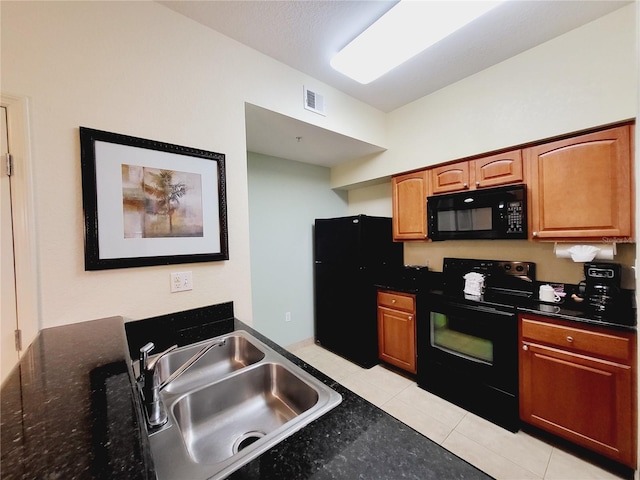 kitchen with visible vents, dark stone counters, light tile patterned floors, black appliances, and a sink