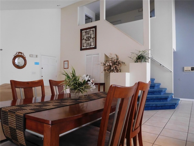 dining area featuring light tile patterned floors, stairway, and a towering ceiling