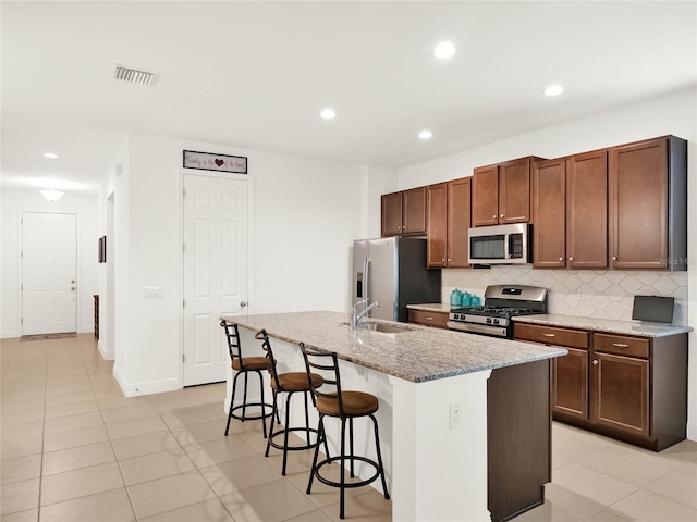 kitchen featuring visible vents, an island with sink, stainless steel appliances, decorative backsplash, and a kitchen breakfast bar