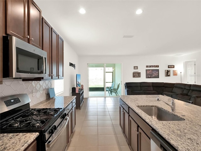 kitchen featuring backsplash, open floor plan, light stone counters, stainless steel appliances, and a sink