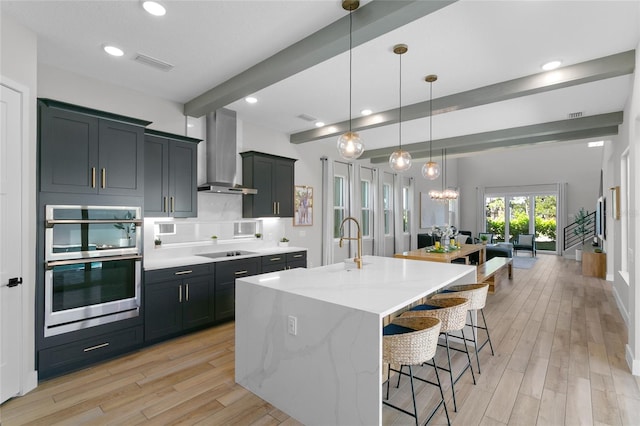 kitchen featuring light wood finished floors, a kitchen bar, double oven, wall chimney exhaust hood, and black electric cooktop