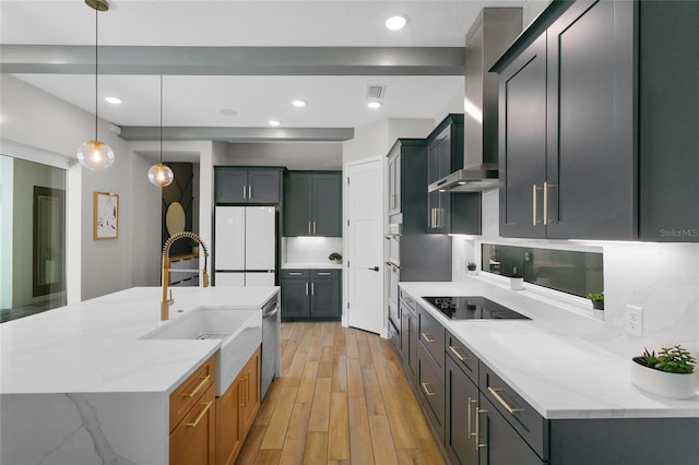 kitchen featuring light wood finished floors, a sink, freestanding refrigerator, wall chimney range hood, and dishwasher