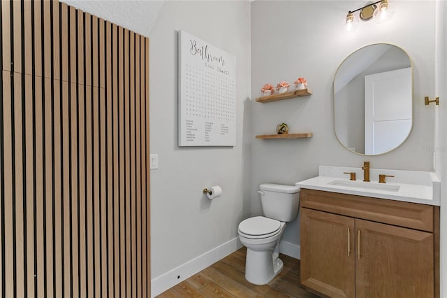 bathroom featuring baseboards, toilet, wood finished floors, and vanity