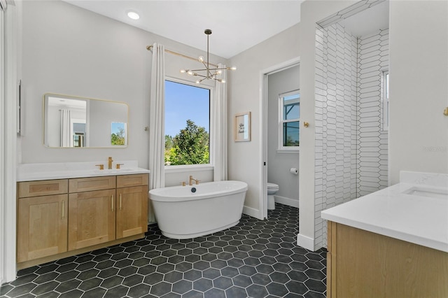 bathroom with baseboards, toilet, a soaking tub, a notable chandelier, and vanity