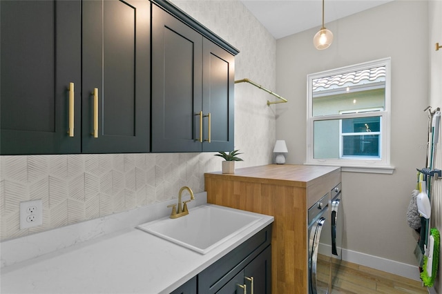 clothes washing area with baseboards, washer and clothes dryer, light wood-type flooring, cabinet space, and a sink