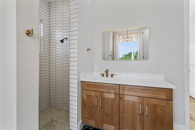 full bath with vanity, an inviting chandelier, and a tile shower