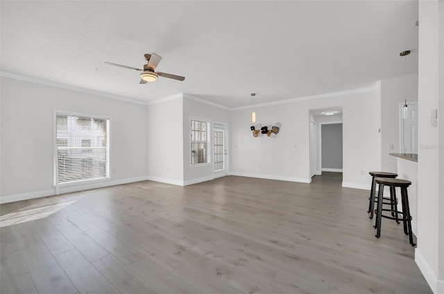 unfurnished living room featuring a healthy amount of sunlight, crown molding, ceiling fan, and wood finished floors