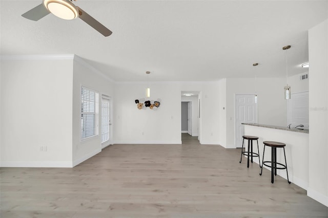 unfurnished living room featuring baseboards, light wood-type flooring, a ceiling fan, and ornamental molding