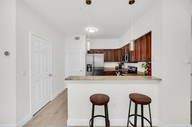 kitchen featuring visible vents, a peninsula, light countertops, appliances with stainless steel finishes, and a kitchen bar