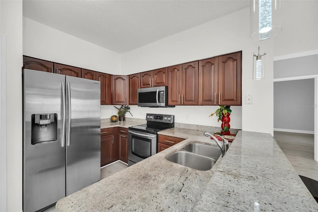 kitchen featuring a sink, light stone countertops, appliances with stainless steel finishes, and light wood-style flooring