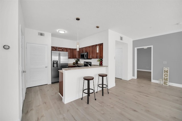 kitchen featuring visible vents, a breakfast bar, a peninsula, light wood-style flooring, and appliances with stainless steel finishes