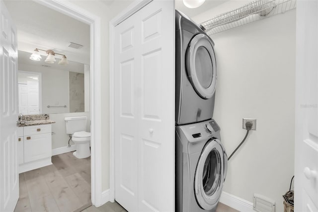 laundry room with baseboards, laundry area, stacked washing maching and dryer, light wood-style floors, and a sink