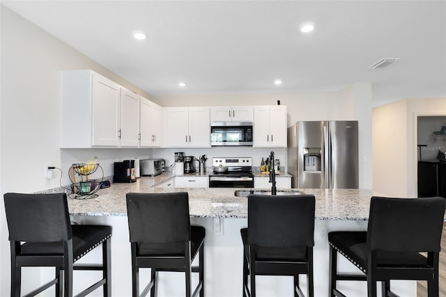 kitchen featuring light stone countertops, visible vents, a peninsula, stainless steel appliances, and white cabinetry