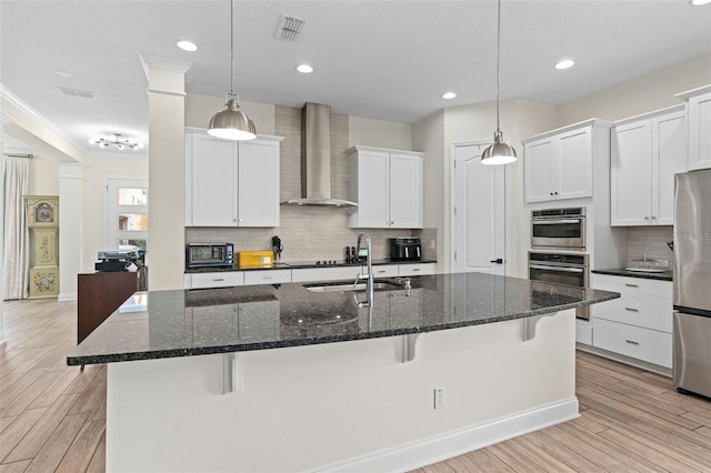 kitchen with visible vents, appliances with stainless steel finishes, light wood-style floors, wall chimney exhaust hood, and a sink