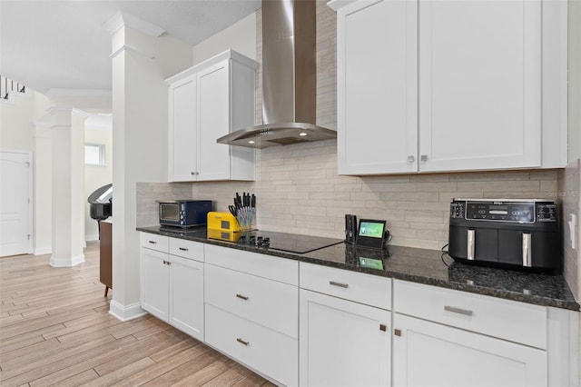 kitchen with decorative columns, light wood-style flooring, white cabinets, black appliances, and wall chimney exhaust hood