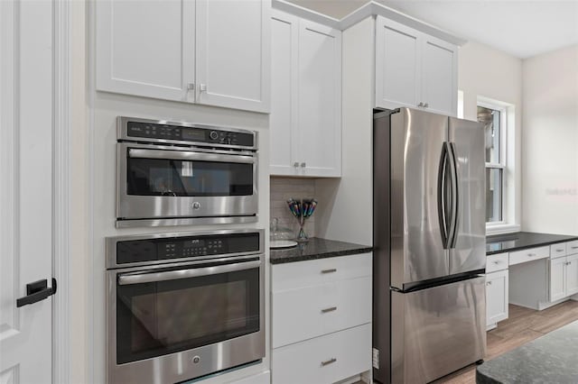 kitchen with light wood-type flooring, appliances with stainless steel finishes, white cabinets, and dark stone counters