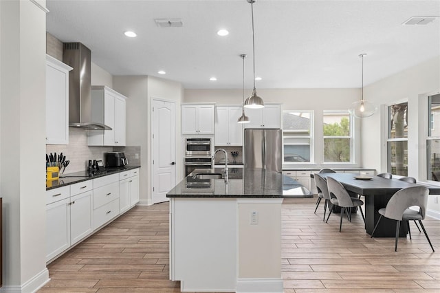 kitchen with visible vents, light wood-style flooring, wall chimney exhaust hood, stainless steel fridge, and backsplash