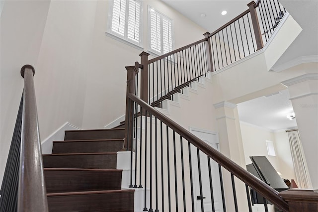 stairway with crown molding, decorative columns, and a towering ceiling