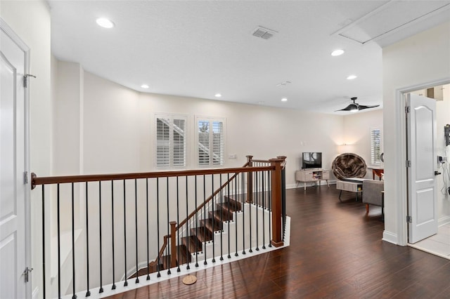 hallway featuring wood finished floors, visible vents, baseboards, recessed lighting, and an upstairs landing