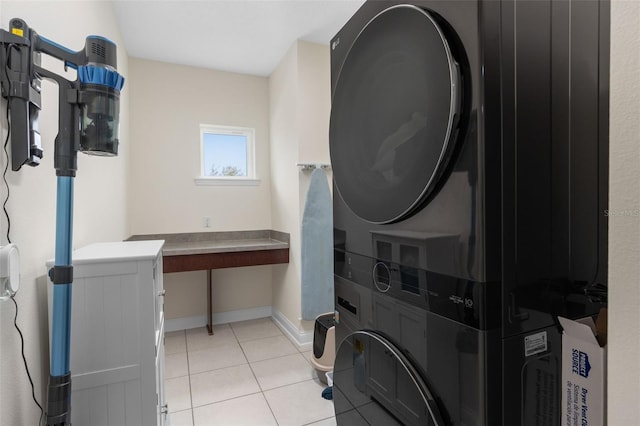 clothes washing area with light tile patterned floors, stacked washer / drying machine, baseboards, and laundry area