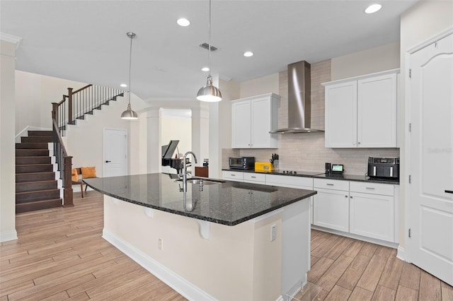 kitchen with tasteful backsplash, wall chimney range hood, light wood-style flooring, white cabinets, and a sink