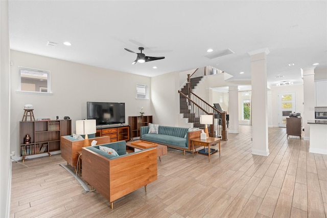 living room with light wood finished floors, stairs, ceiling fan, and decorative columns