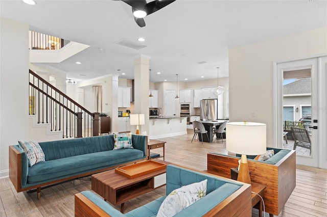 living area featuring recessed lighting, light wood-type flooring, ornate columns, and stairway