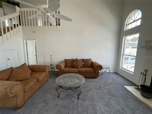 carpeted living room with ceiling fan, stairway, baseboards, and a towering ceiling