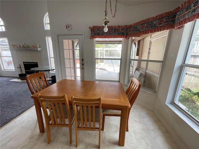 dining space featuring baseboards, light colored carpet, a towering ceiling, and a fireplace