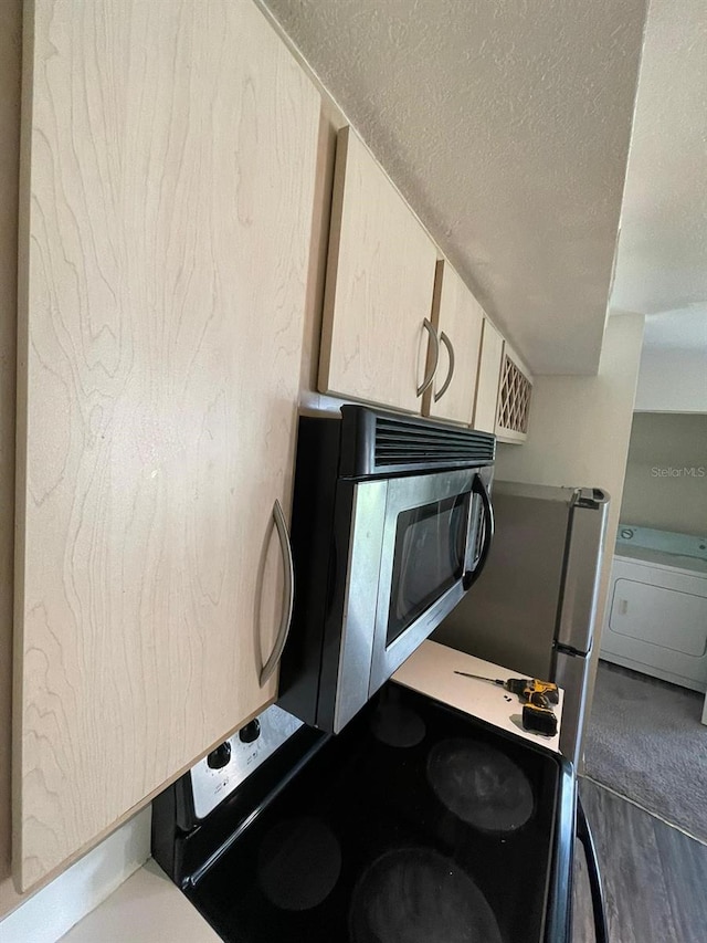 kitchen featuring stainless steel microwave, washer / dryer, a textured ceiling, and light countertops