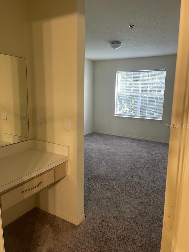 interior space featuring baseboards, a textured ceiling, and dark carpet