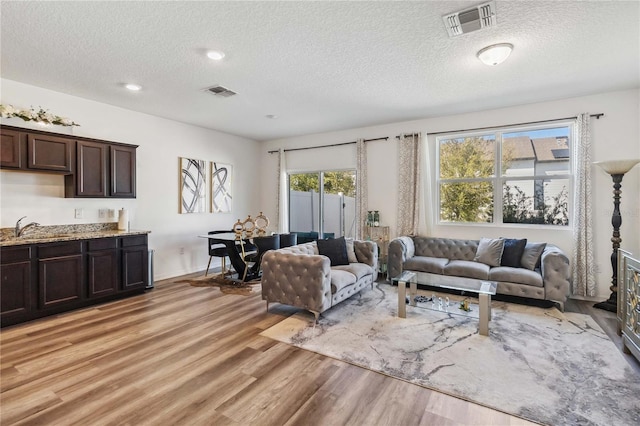 living room with visible vents, light wood-style floors, and a textured ceiling