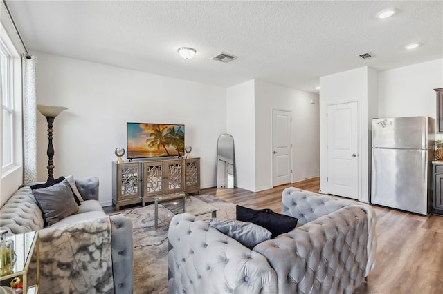 living area featuring light wood finished floors, visible vents, and a textured ceiling