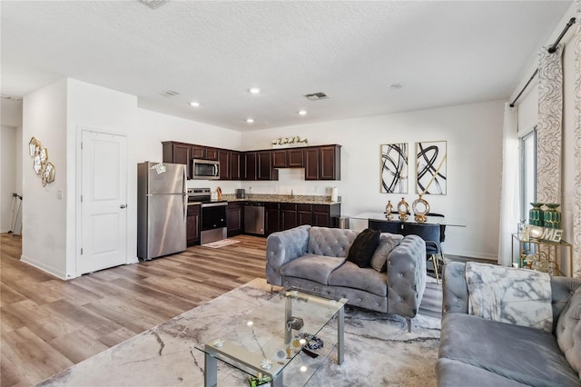 living area with visible vents, baseboards, light wood-type flooring, recessed lighting, and a textured ceiling