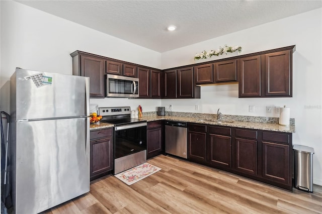 kitchen with a sink, light wood-style flooring, dark brown cabinets, and stainless steel appliances